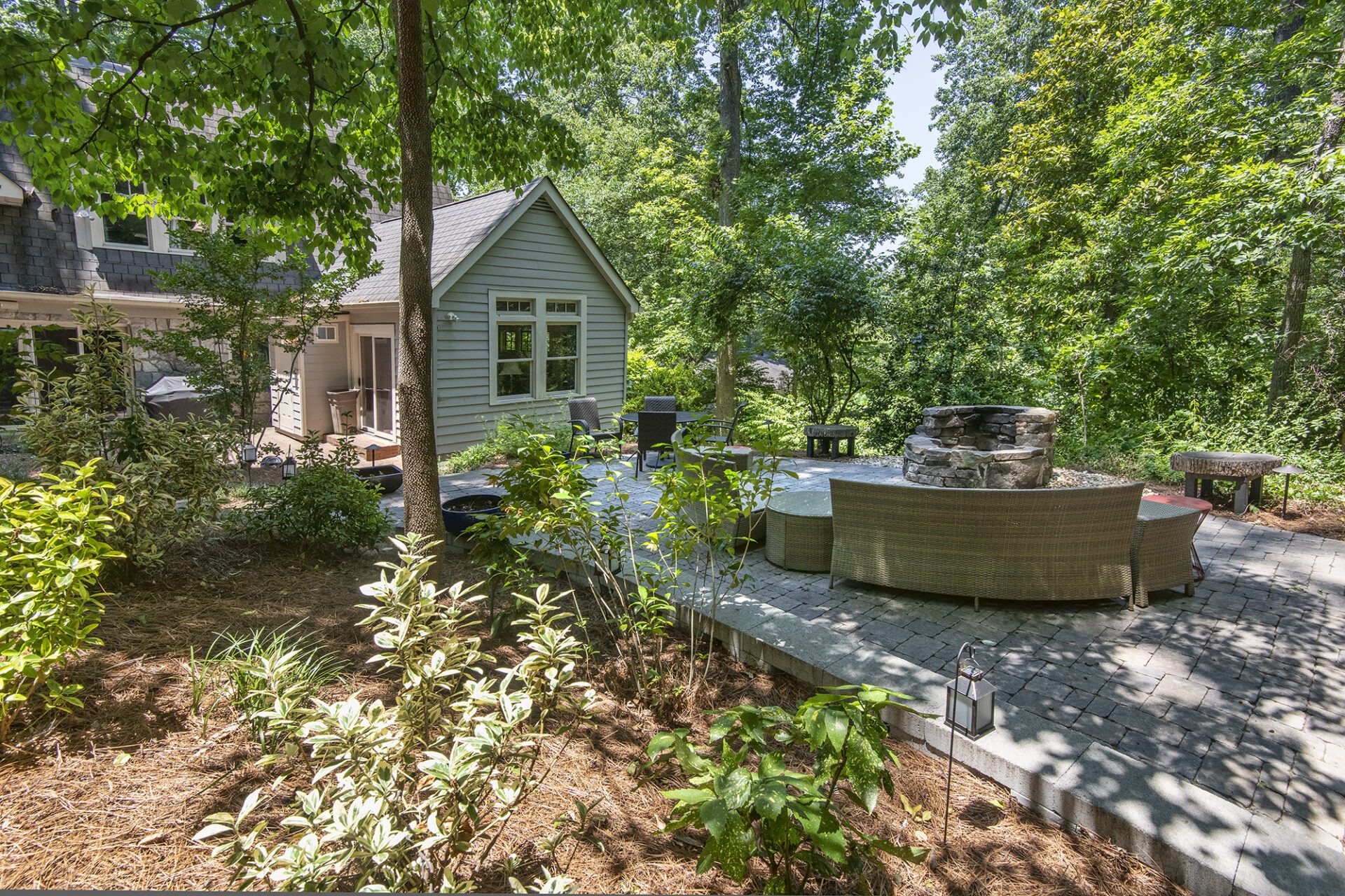 A cozy backyard patio with wicker furniture and fire pit, surrounded by lush trees and greenery, providing a peaceful, inviting atmosphere.