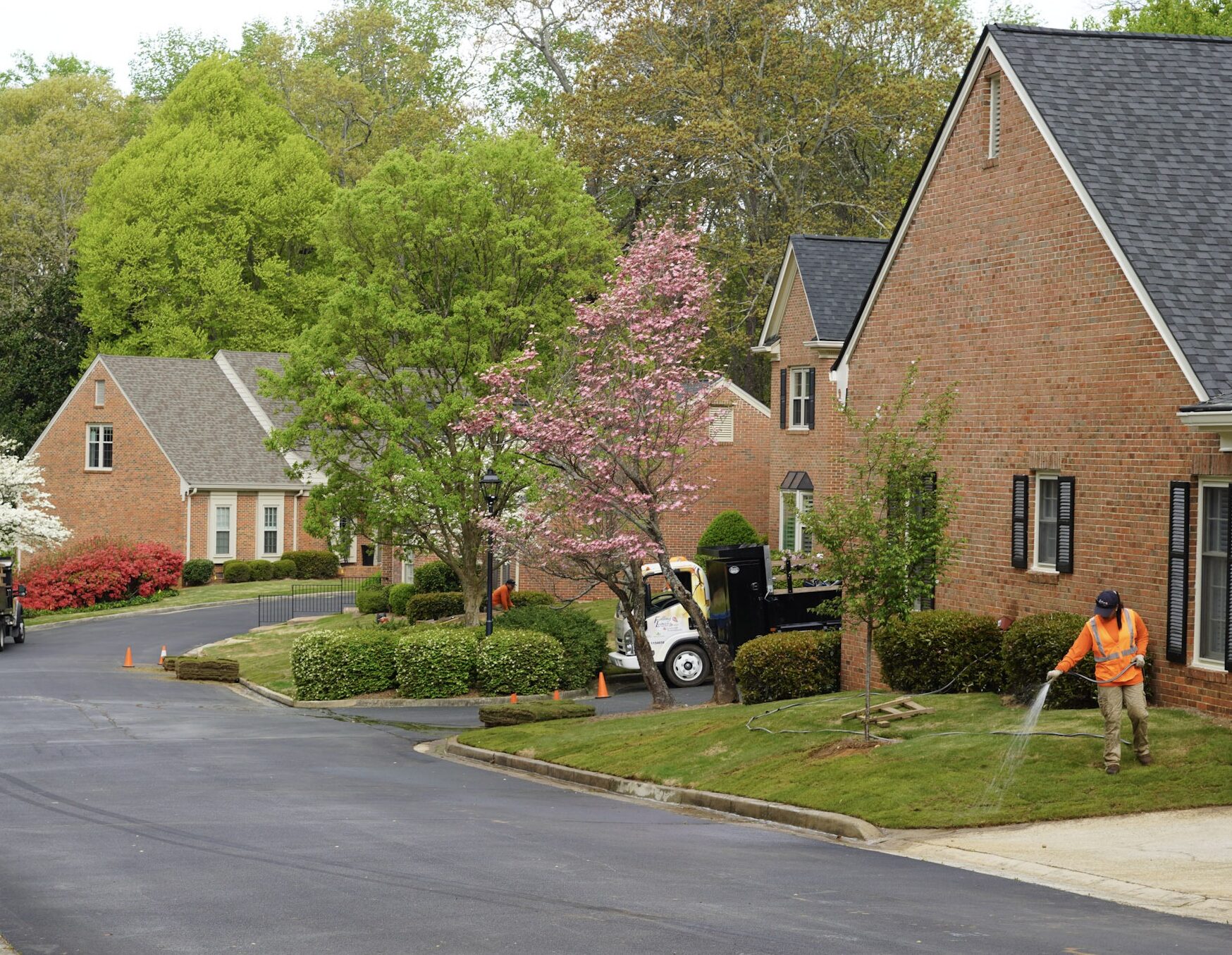Landscape crew members water green grass with colorful Spring blooms in the background