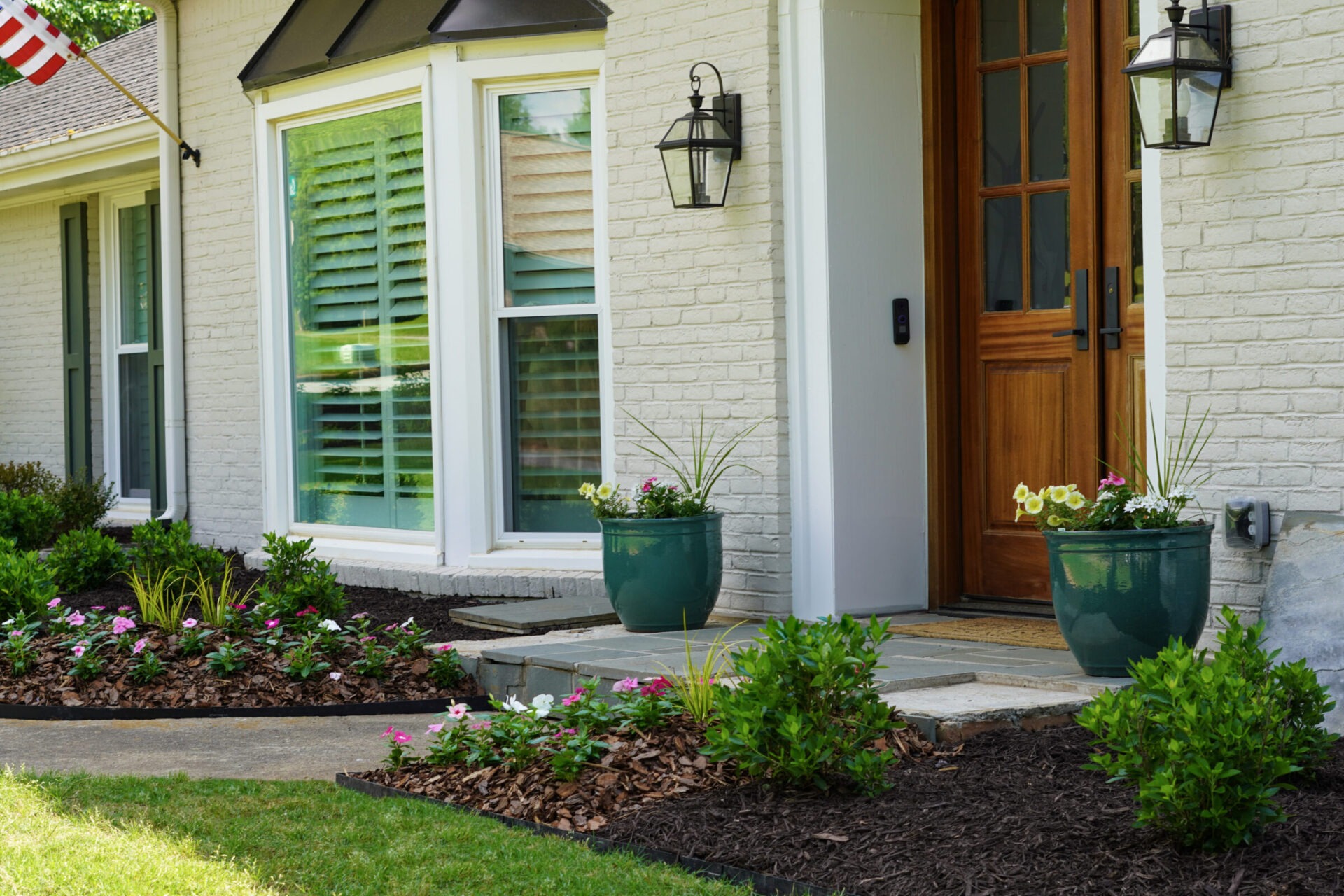 Pink spring flowers in brown mulch in front of a white brick house with a brown front door.