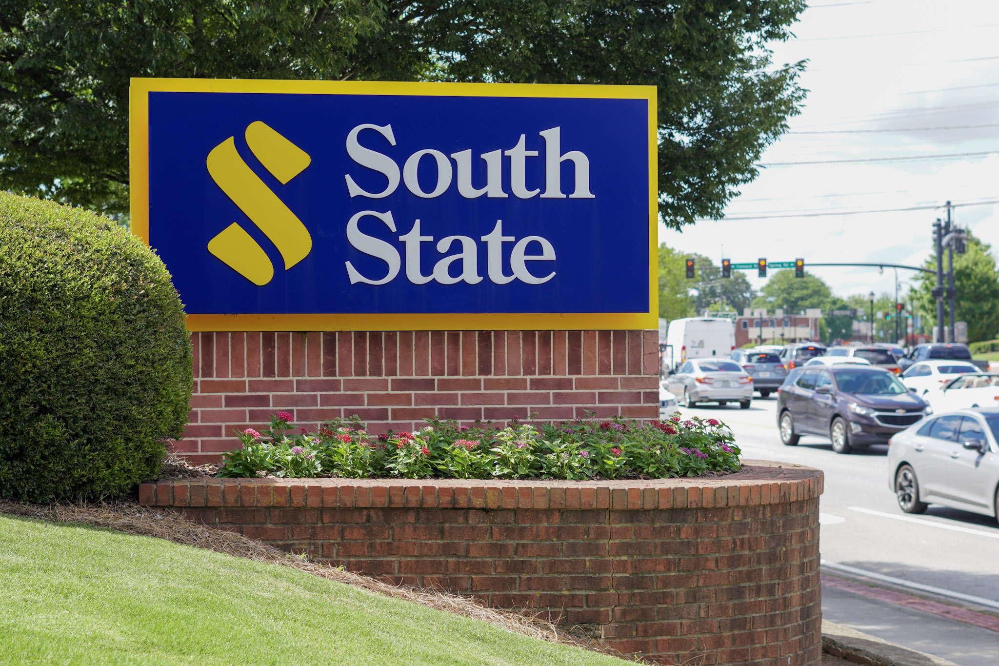 Retail location sign above brick retaining wall with colorful flowers blooming